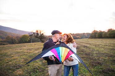 Ein älterer Mann und eine Frau halten einen Drachen in der herbstlichen Natur bei Sonnenuntergang und schauen sich an. - HPIF27586