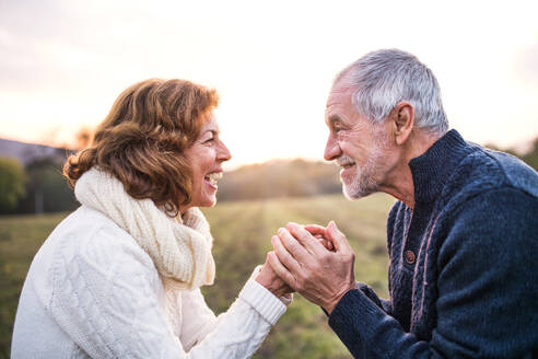 Älteres Paar, das sich auf einer Wiese in herbstlicher Natur anschaut und die Hände hält. - HPIF27596