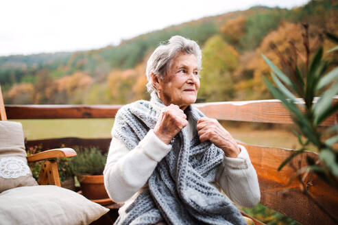 An elderly senior woman sitting outdoors on a terrace in on a sunny day in autumn. - HPIF27606