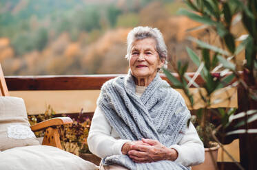 Eine ältere Seniorin sitzt an einem sonnigen Herbsttag auf einer Terrasse im Freien. - HPIF27608