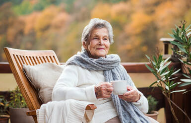 Eine ältere Seniorin sitzt an einem sonnigen Herbsttag auf einer Terrasse im Freien. - HPIF27617