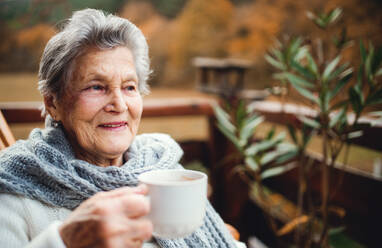 Eine ältere Seniorin steht an einem sonnigen Herbsttag auf einer Terrasse im Freien. - HPIF27622