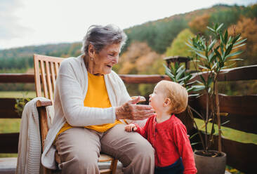 An elderly woman sitting with a toddler great-grandchild on a terrace on a sunny day in autumn. - HPIF27648