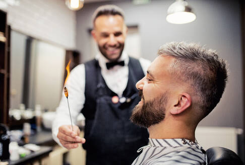 Gutaussehender Hipster-Mann, der einen Friseur und eine Friseurin im Friseursalon besucht, Ohrhaarentfernung. - HPIF27679