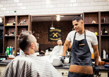 Ein reifer Mann im Gespräch mit einem Friseur und einer Friseurin in einem Friseursalon. - HPIF27683