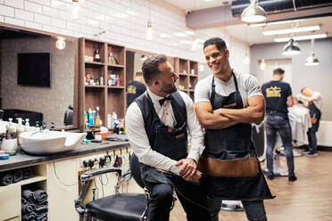 Zwei männliche Friseure und Hairstylisten sitzen in einem Friseursalon und posieren für ein Foto. - HPIF27694