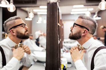 Gutaussehender Hipster-Kunde mit Brille, der in den Spiegel eines Friseursalons schaut. - HPIF27699