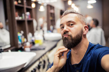 Gutaussehender Hipster-Kunde, der einen Friseur und einen Haarstylisten im Friseursalon besucht und dabei lustige Gesichter macht. - HPIF27727