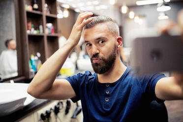 A hipster man client in barber shop, making funny faces when taking seflie. - HPIF27728