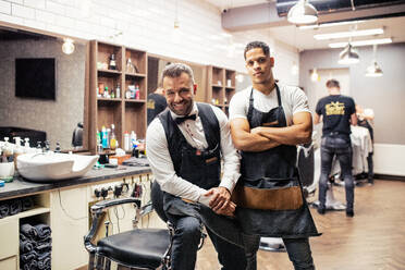 Two male haidressers and hairstylists sitting in barber shop, posing for a photograph. - HPIF27732