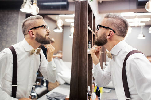 Gutaussehender Hipster-Kunde mit Brille, der in den Spiegel eines Friseursalons schaut. - HPIF27735