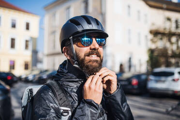 Männlicher Hipster-Kurier, der in der Stadt einen Helm aufsetzt und Pakete ausliefert, Kopierraum. - HPIF27737