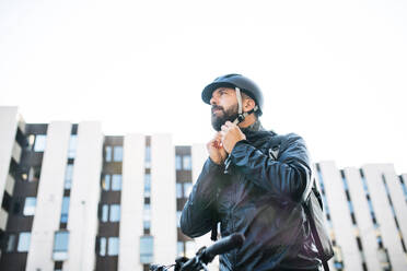 Männlicher Kurier mit Fahrrad, der beim Ausliefern von Paketen in der Stadt einen Helm aufsetzt, Kopierraum. - HPIF27740