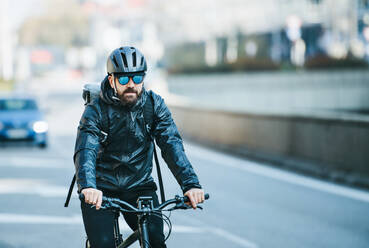 Vorderansicht eines männlichen Fahrradkuriers mit Sonnenbrille, der in der Stadt radelt und Pakete ausliefert; Kopierraum. - HPIF27744