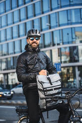 Ein Porträt eines männlichen Fahrradkuriers mit Rucksack, der Pakete in der Stadt ausliefert. - HPIF27747