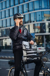 Männlicher Hipster-Kurier mit Fahrrad auf einer Straße in der Stadt, der beim Ausliefern von Paketen telefoniert. - HPIF27748