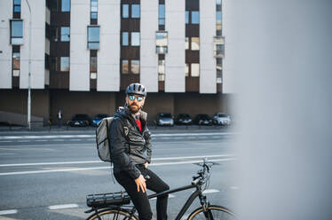 Ein Porträt eines männlichen Fahrradkuriers mit Rucksack, der Pakete in der Stadt ausliefert. - HPIF27749