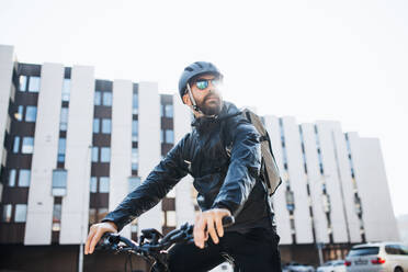 Männlicher Kurier mit Fahrrad und Sonnenbrille, der Pakete in der Stadt ausliefert. Kopierraum. - HPIF27750
