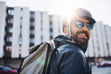 Männlicher Kurier mit Sonnenbrille, der Pakete in der Stadt ausliefert, Kopierraum. - HPIF27752