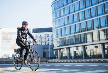 Ein männlicher Fahrradkurier mit Sonnenbrille radelt durch die Stadt, um Pakete auszuliefern. Kopierraum. - HPIF27757