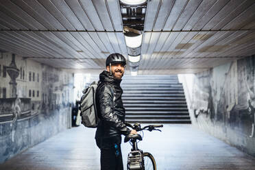 Männlicher Fahrradkurier, der in der U-Bahn steht, wenn er Pakete in der Stadt ausliefert, Kopierraum. - HPIF27758
