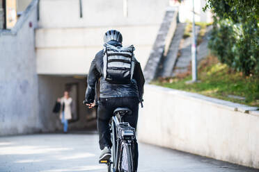 Rückansicht eines männlichen Fahrradkuriers, der in der Stadt Pakete ausliefert, Kopierraum. - HPIF27762