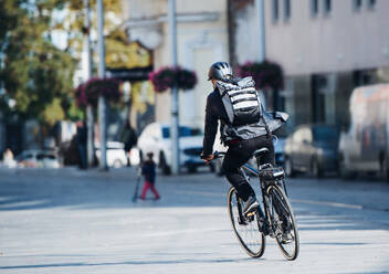 Rückansicht eines männlichen Fahrradkuriers, der in der Stadt Pakete ausliefert, Kopierraum. - HPIF27774