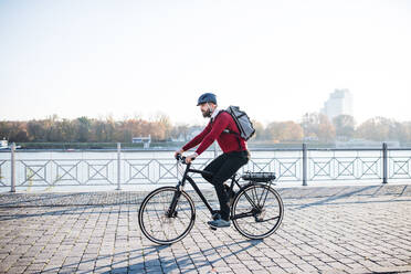 A side view of hipster businessman commuter with electric bicycle traveling to work in city. Copy space. - HPIF27793
