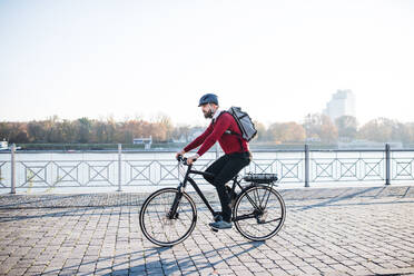 Seitenansicht eines Hipster-Geschäftsmannes mit Elektrofahrrad auf dem Weg zur Arbeit in der Stadt. Raum kopieren. - HPIF27793