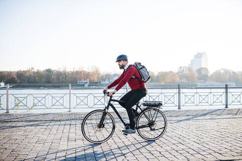 Seitenansicht eines Hipster-Geschäftsmannes mit Elektrofahrrad auf dem Weg zur Arbeit in der Stadt. Raum kopieren. - HPIF27793