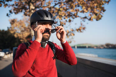 Hipster Geschäftsmann mit Fahrradhelm auf dem Weg zur Arbeit in der Stadt, Sonnenbrille aufsetzend. - HPIF27796