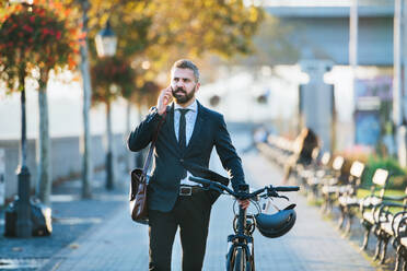 Ein Geschäftsmann mit Fahrrad auf dem Heimweg von der Arbeit in der Stadt, der sein Smartphone benutzt. - HPIF27810