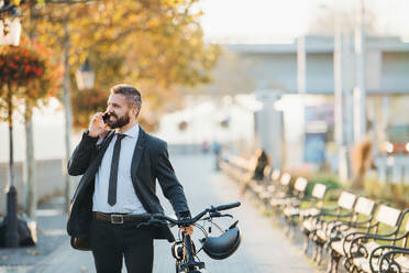 Ein Geschäftsmann mit Fahrrad auf dem Heimweg von der Arbeit in der Stadt, der sein Smartphone benutzt. - HPIF27811
