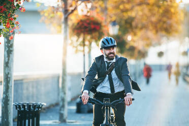 Hipster businessman commuter with electric bicycle traveling home from work in city at sunset. Copy space. - HPIF27815