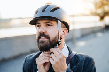 Hipster-Geschäftsmann, der auf dem Heimweg von der Arbeit in der Stadt einen Fahrradhelm aufsetzt. - HPIF27816