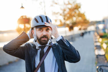 Hipster-Geschäftsmann, der auf dem Heimweg von der Arbeit in der Stadt einen Fahrradhelm aufsetzt. - HPIF27818