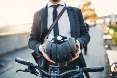 Midsection of businessman commuter with electric bicycle traveling home from work in city, holding a helmet. - HPIF27819