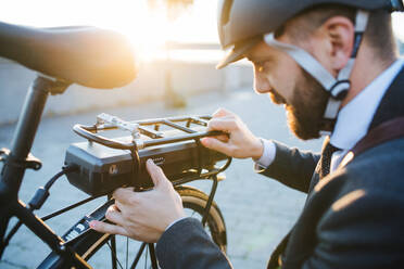 Hipster businessman commuter setting up electric bicycle when traveling home from work in city. - HPIF27821