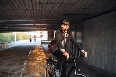 A front view of hipster businessman commuter with electric bicycle traveling to work in city. Copy space. - HPIF27827