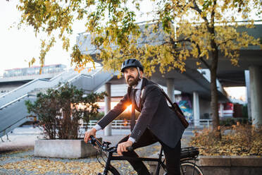 Hipster businessman commuter with electric bicycle traveling home from work in city at sunset. Copy space. - HPIF27829