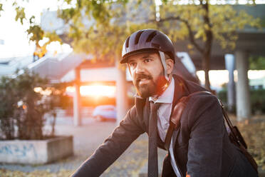 Hipster Geschäftsmann mit Fahrrad auf dem Heimweg von der Arbeit in der Stadt bei Sonnenuntergang. Kopierraum. - HPIF27830