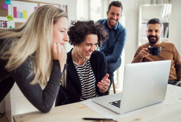 Group of young cheerful male and female businesspeople with laptop working together in a modern office. - HPIF27834