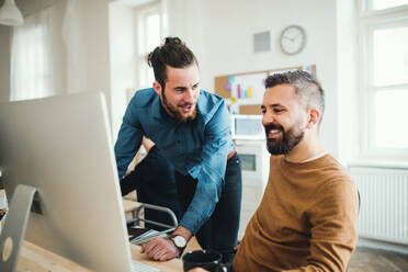 Zwei junge männliche Geschäftsleute mit Computern unterhalten sich in einem modernen Büro. - HPIF27842