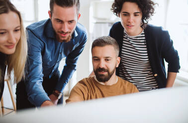 Group of young,cheerful, male and female businesspeople looking at laptop screen in a modern office, discussing issues. - HPIF27844