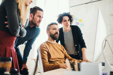 Group of young concentrated male and female businesspeople with computer working together in a modern office. - HPIF27845