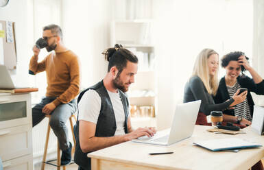Eine Gruppe junger, konzentrierter Geschäftsleute mit Laptop und Smartphone arbeitet in einem modernen Büro. - HPIF27853