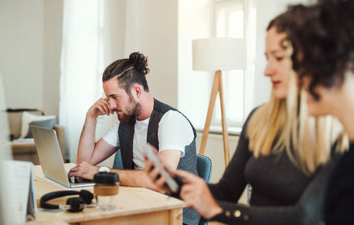 Eine Gruppe junger, fröhlicher Geschäftsleute mit Smartphone und Laptop arbeitet in einem modernen Büro zusammen. - HPIF27854