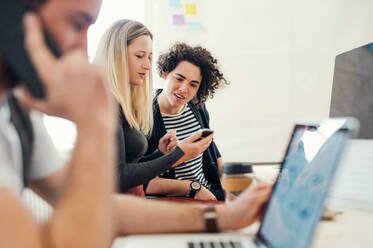 Group of young concentrated male and female businesspeople with laptop and smartphone working together in a modern office. - HPIF27858