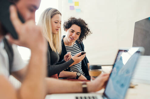 Eine Gruppe von jungen, konzentrierten Geschäftsleuten mit Laptop und Smartphone arbeitet in einem modernen Büro zusammen. - HPIF27858