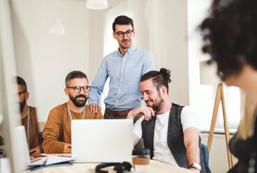 Eine Gruppe junger, fröhlicher Geschäftsleute sitzt in einem modernen Büro um einen Tisch herum und hält eine Besprechung ab. - HPIF27864